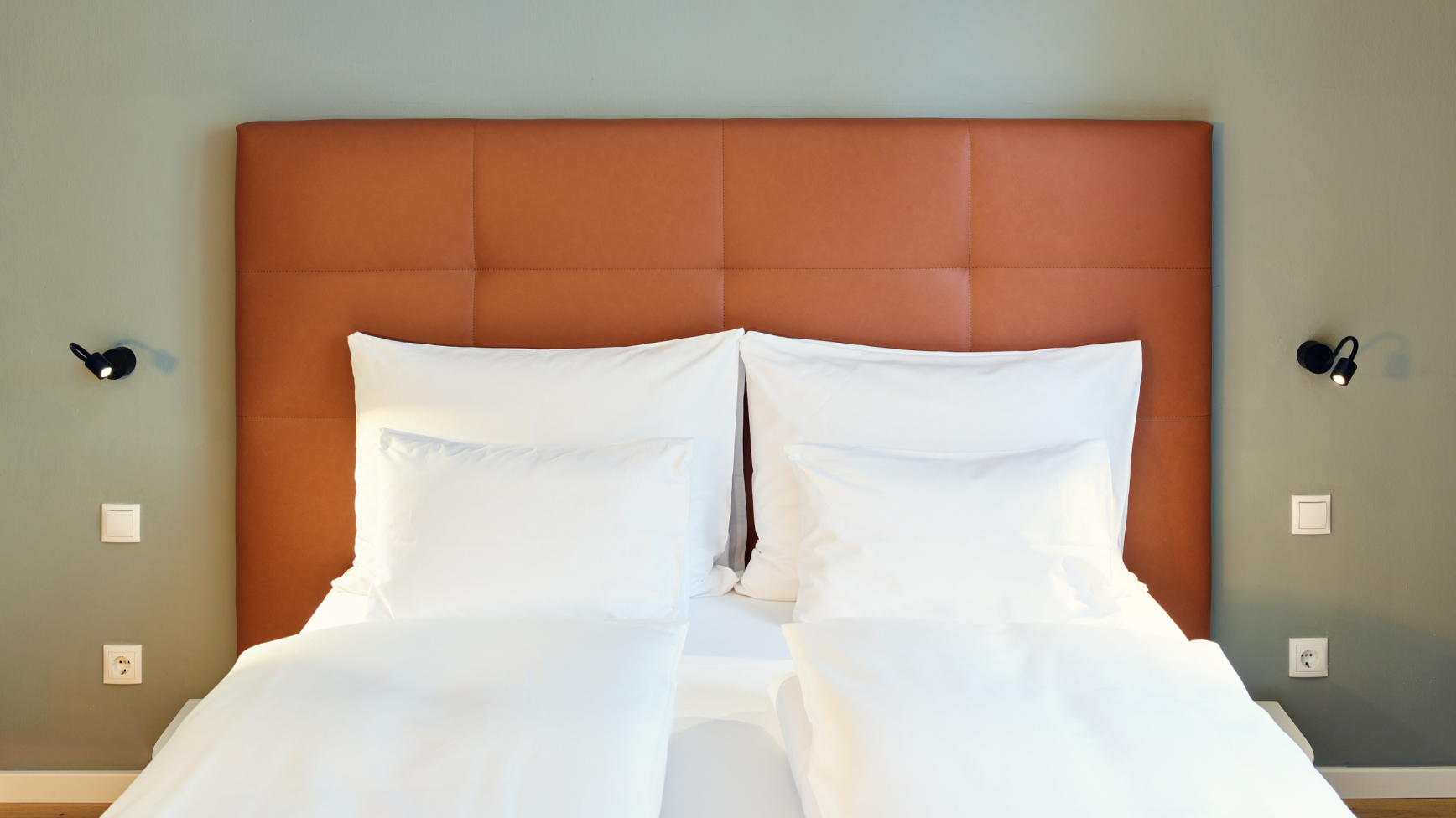 Nahaufnahme eines Doppelbetts mit weißer Bettwäsche und einem braunen, gesteppten Kopfteil.