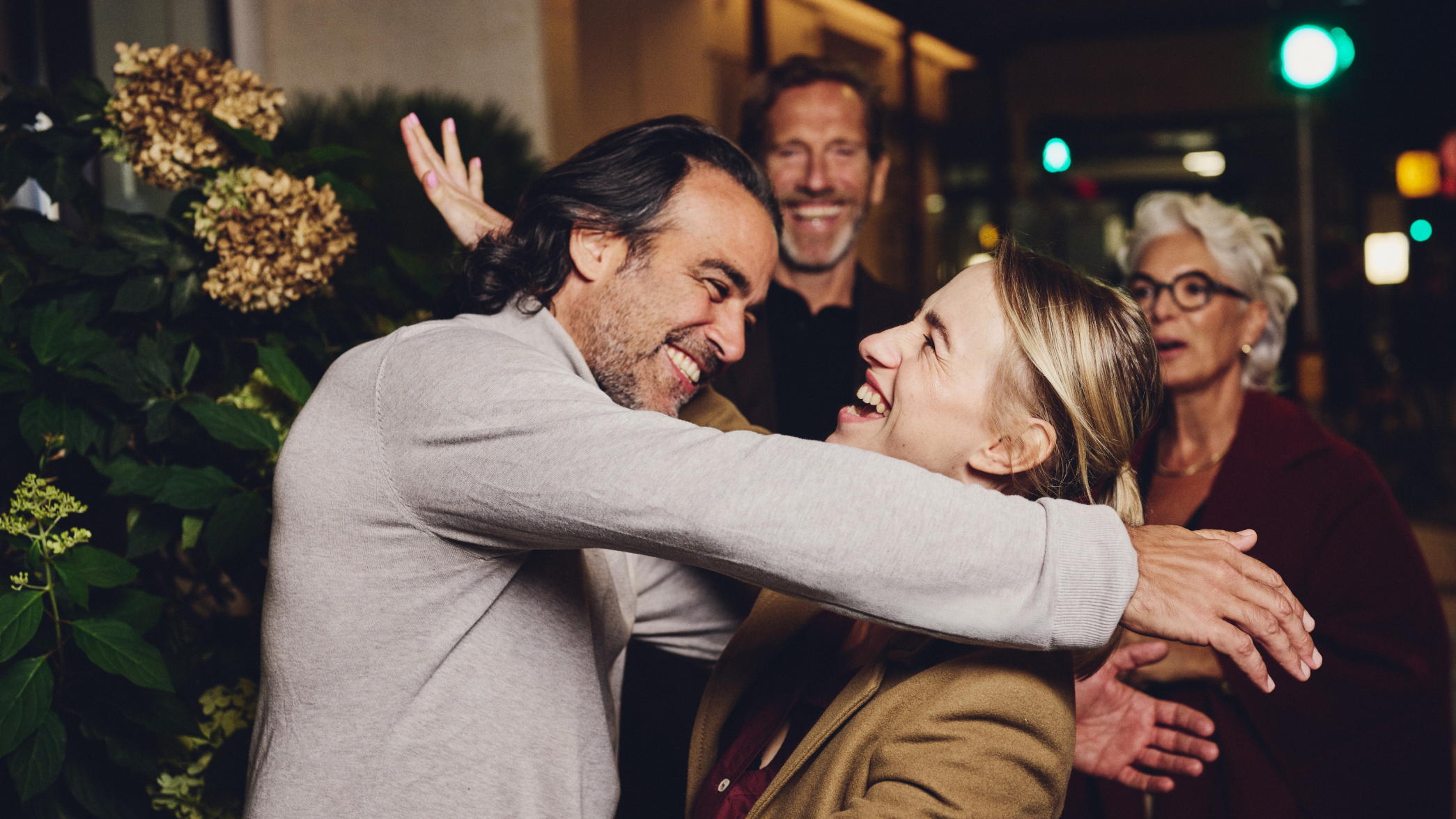 Eine lächelnde Frau umarmt einen Mann, während andere lächeln und zusehen.