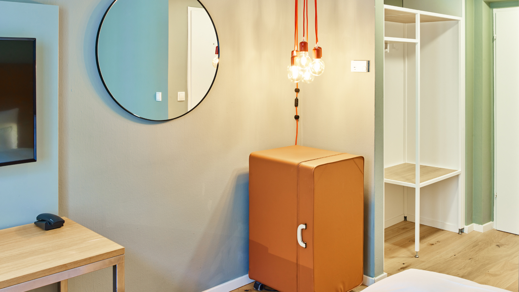 Ein Hotelzimmer mit einem Spiegel, einer Lampe, einem Mini-Kühlschrank und einem offenen Kleiderschrank.