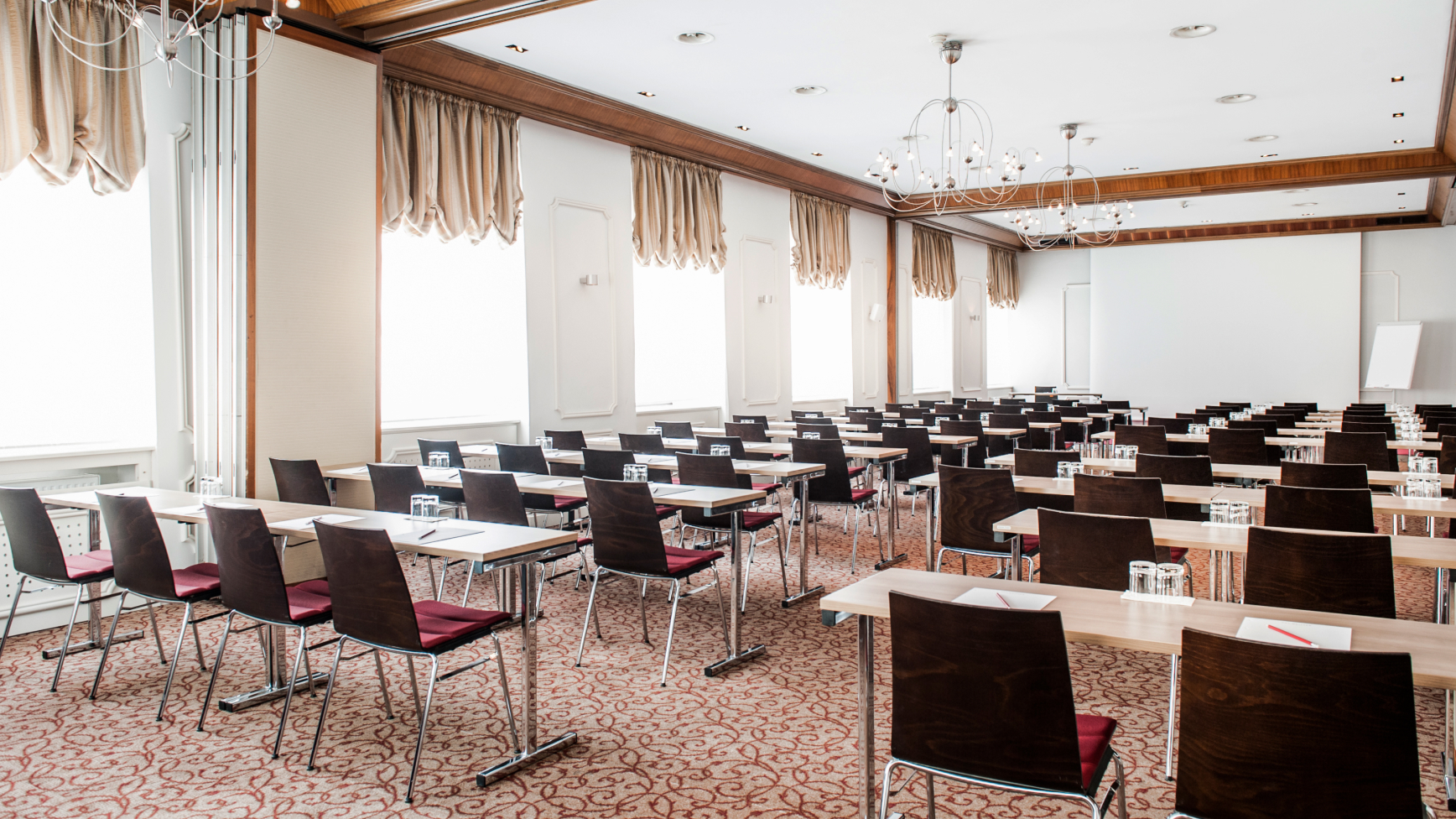 Ein heller Konferenzraum mit Tischen und Stühlen, einem Teppich und Fenstern.