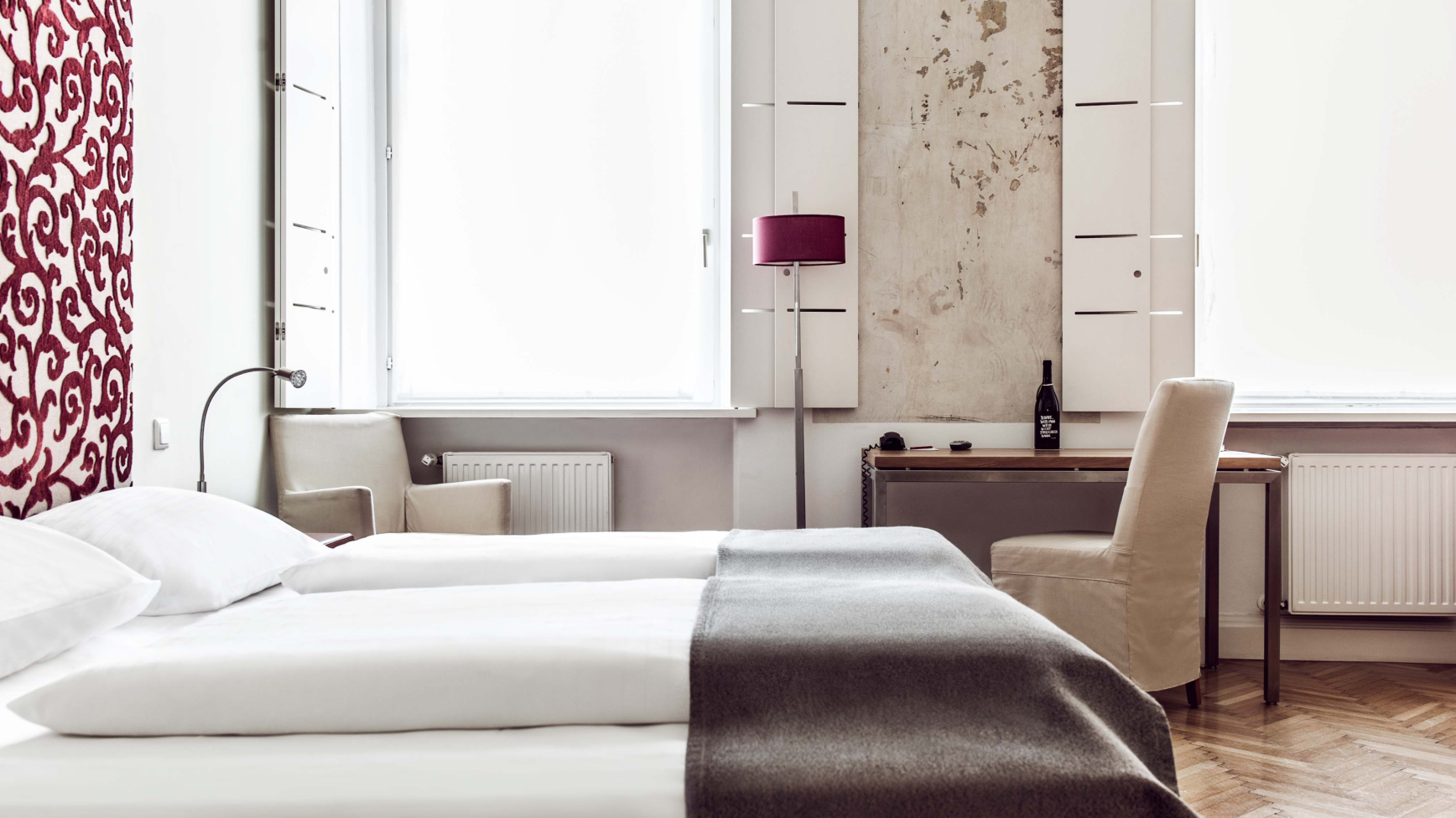 Schlafzimmer mit zwei Einzelbetten, roter Akzentwand, Schreibtisch und Stuhl unter dem Fenster.