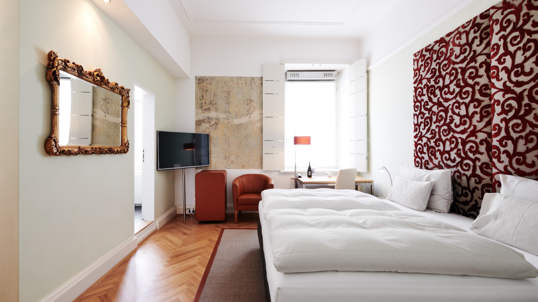 Ein Schlafzimmer mit Spiegel, Fernseher, Bett, Schreibtisch und roter Akzentwand.