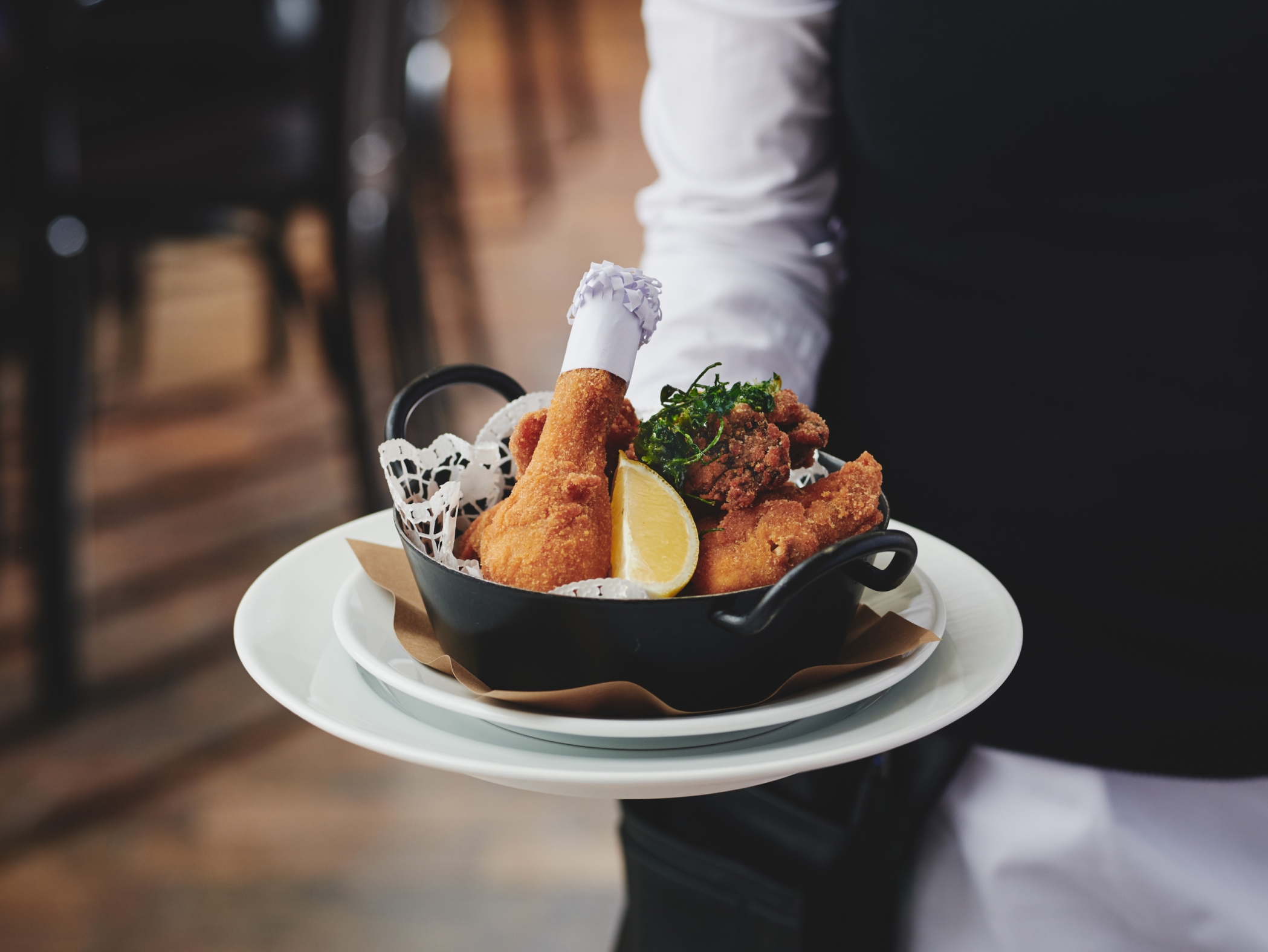 Ein Kellner serviert gebratenes Huhn in einem schwarzen Gericht auf einem weißen Teller mit Zitrone.