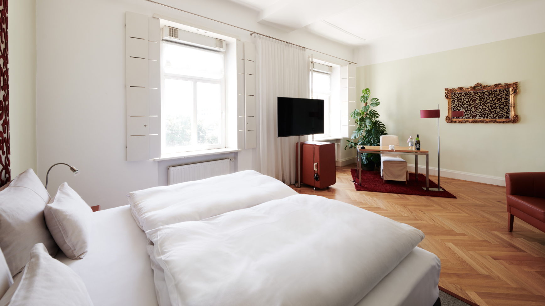 Helles Hotelzimmer mit großem Bett, Fernseher, Schreibtisch und Kunstwerk.