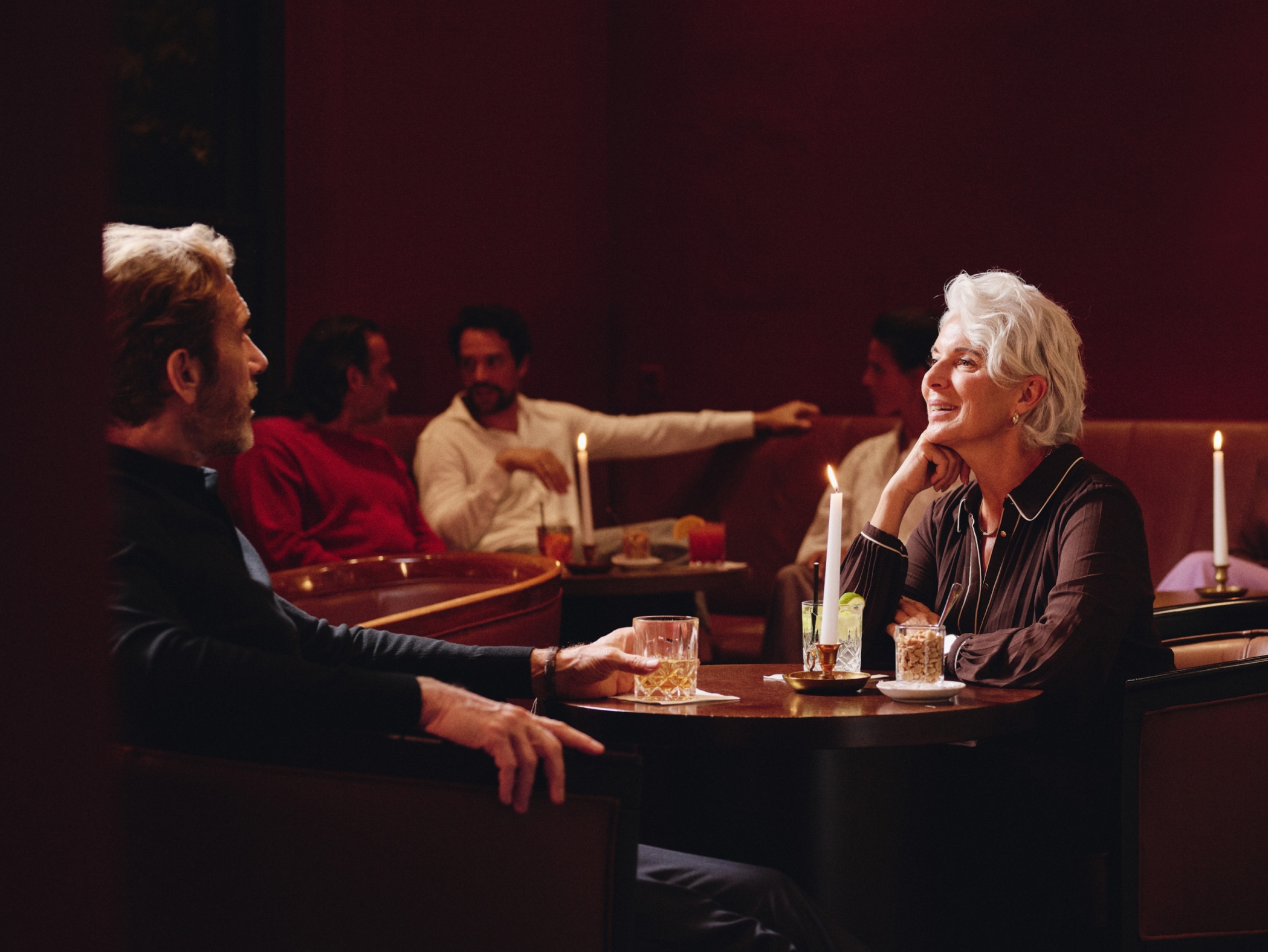 Ein Mann und eine Frau trinken Cocktails an einem Tisch, andere Leute im Hintergrund.