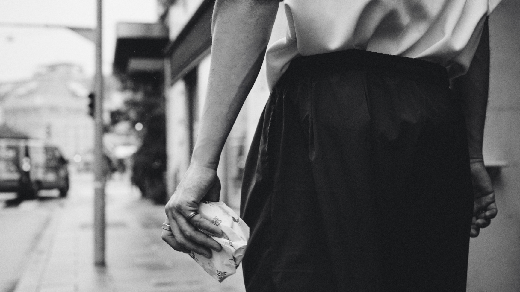 Eine Person mit zerknittertem Papier in der Hand, die in Schwarzweiß in der Stadt geht.
