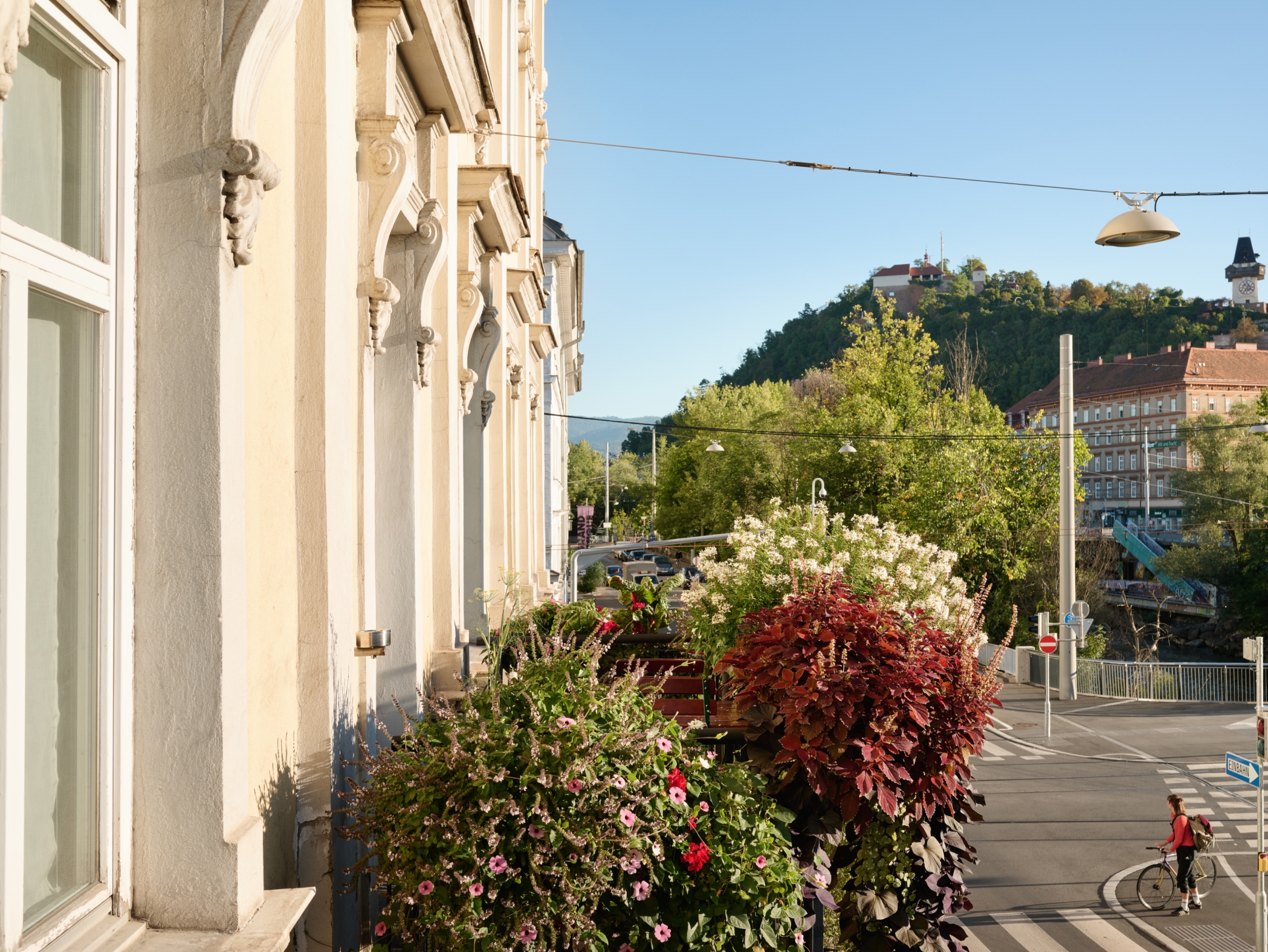 Aussicht vom Balkon in Graz, Österreich, auf den Schlossberg und die Stadt mit Radfahrerin.