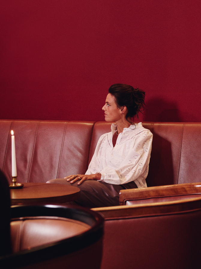 Eine Frau sitzt auf einem Ledersofa mit einem roten Hintergrund und einem Tisch mit einer Kerze.