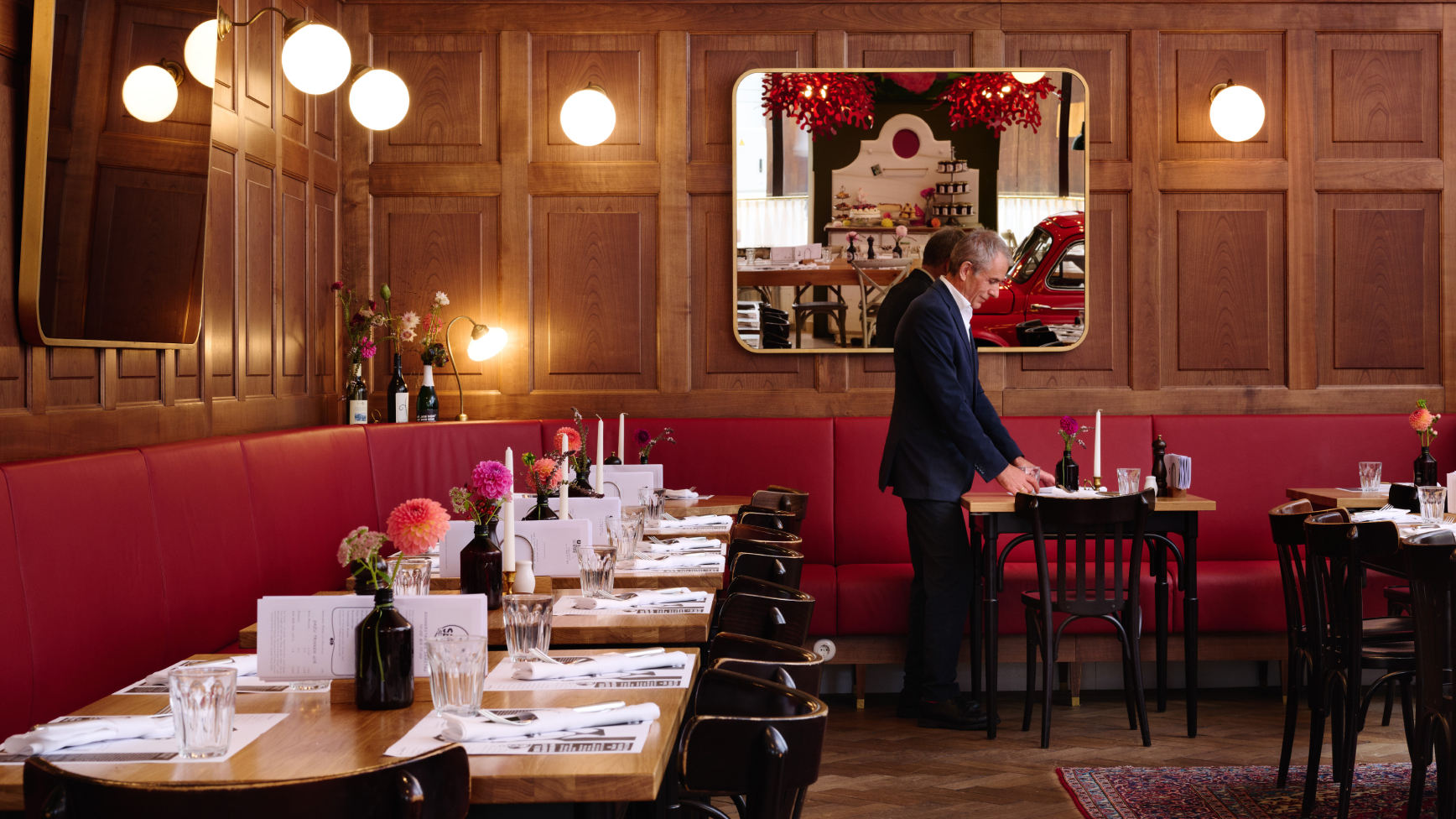 Innenraum eines Restaurants mit Holzvertäfelung, roter Sitzbank und einem Mann, der einen Tisch deckt.