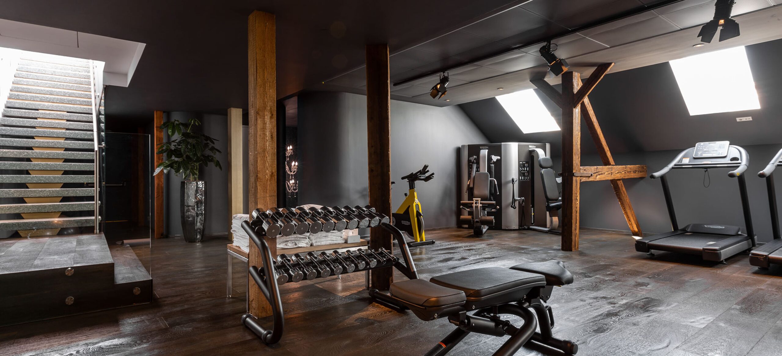 Dumbbells, treadmill, and exercise equipment in an indoor gym with wood beams.