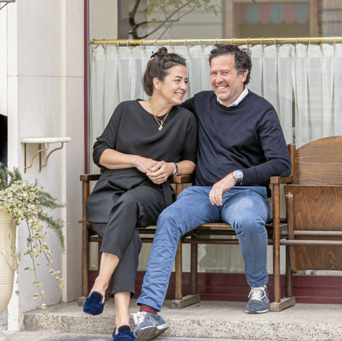 Astrid and Florian Weitzer smiling on a bench in front of Der Steirer restaurant.