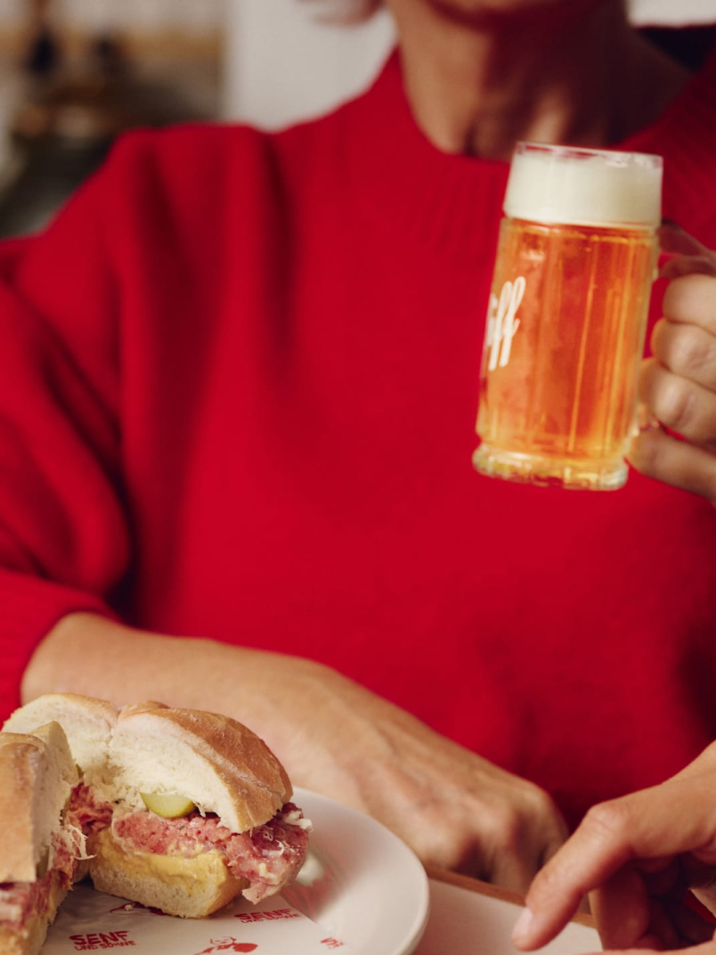A table with SENE sandwiches, a person holding a beer, and another person pointing.