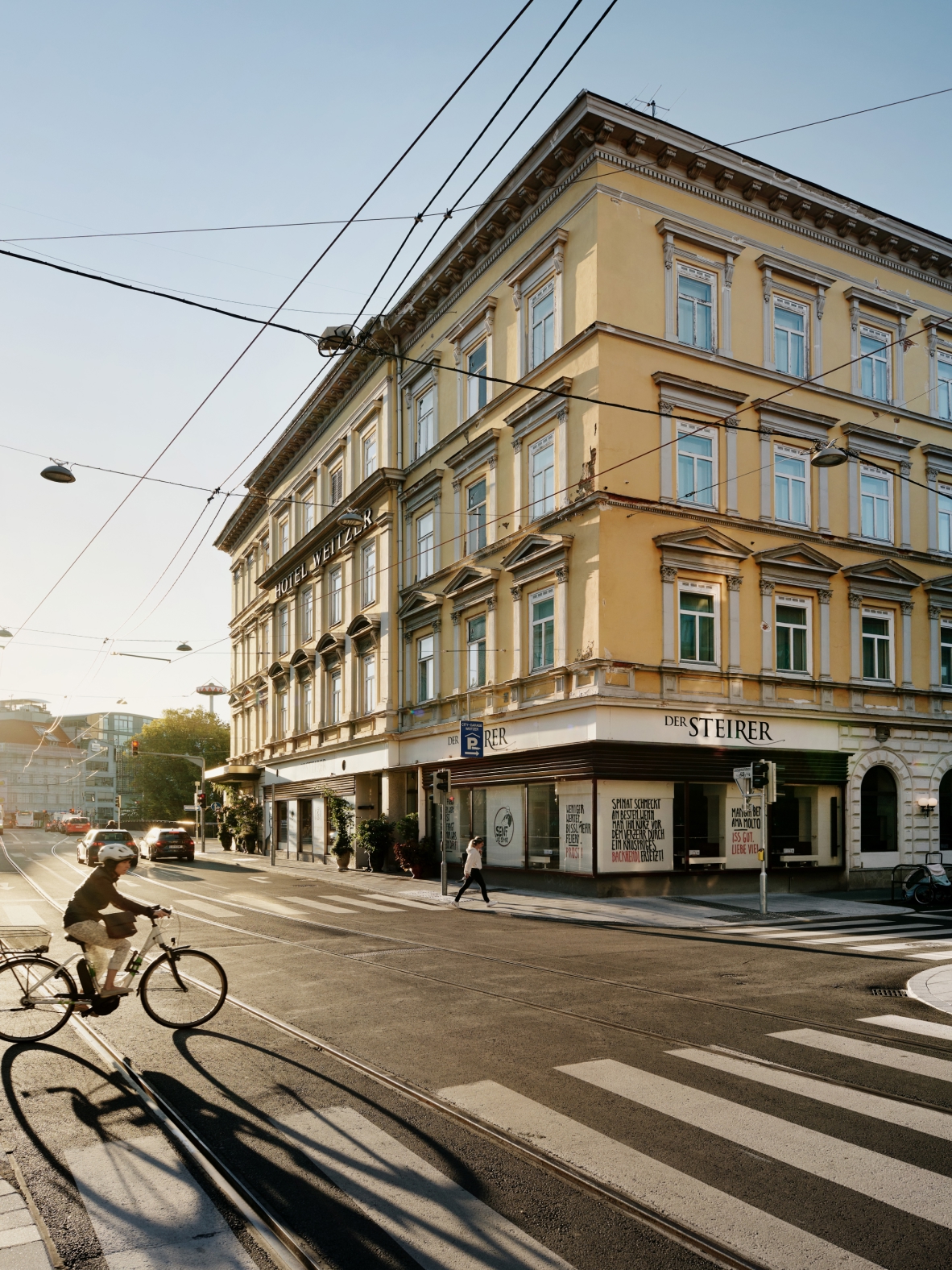 Ansicht des Hotels Weitzer und des Restaurants Der Steirer in Graz, Österreich, mit Radfahrer und Fußgänger.