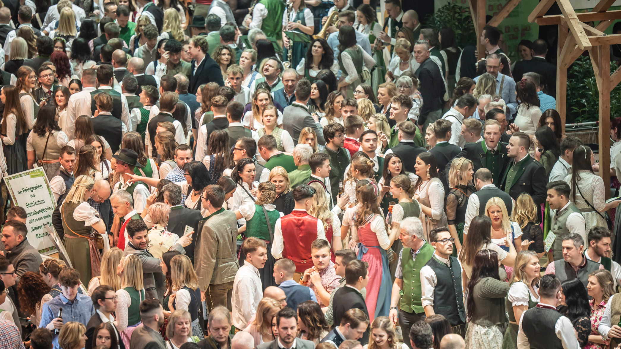 Crowd in traditional dress with musicians. Text: "Proceeds from the Steirischer Bauernbundball go to Steirer helfen Steirern."