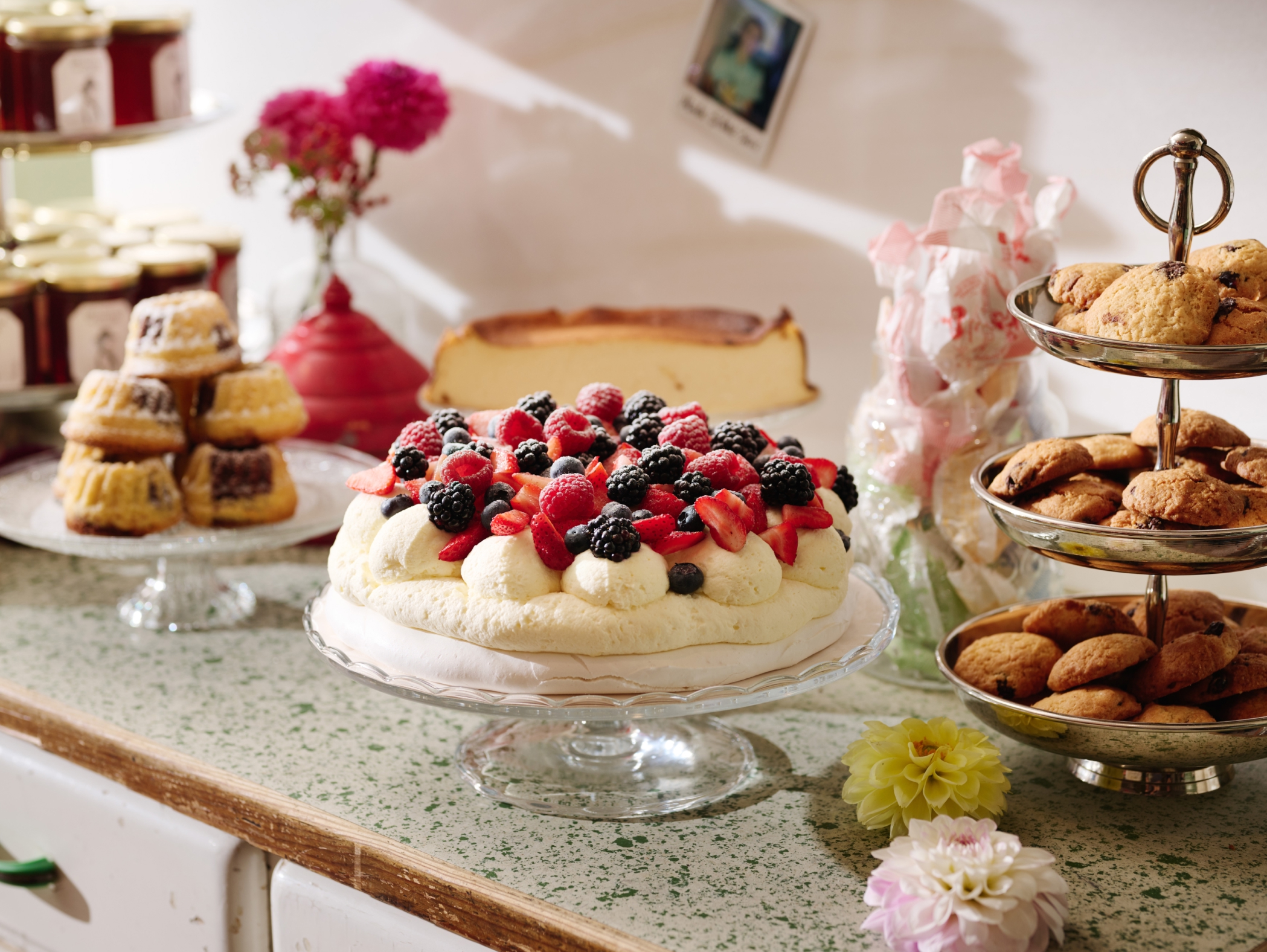 Ein Tisch mit Kuchen, Keksen und Marmeladengläsern. Der Kuchen ist mit Beeren und Schlagsahne belegt.
