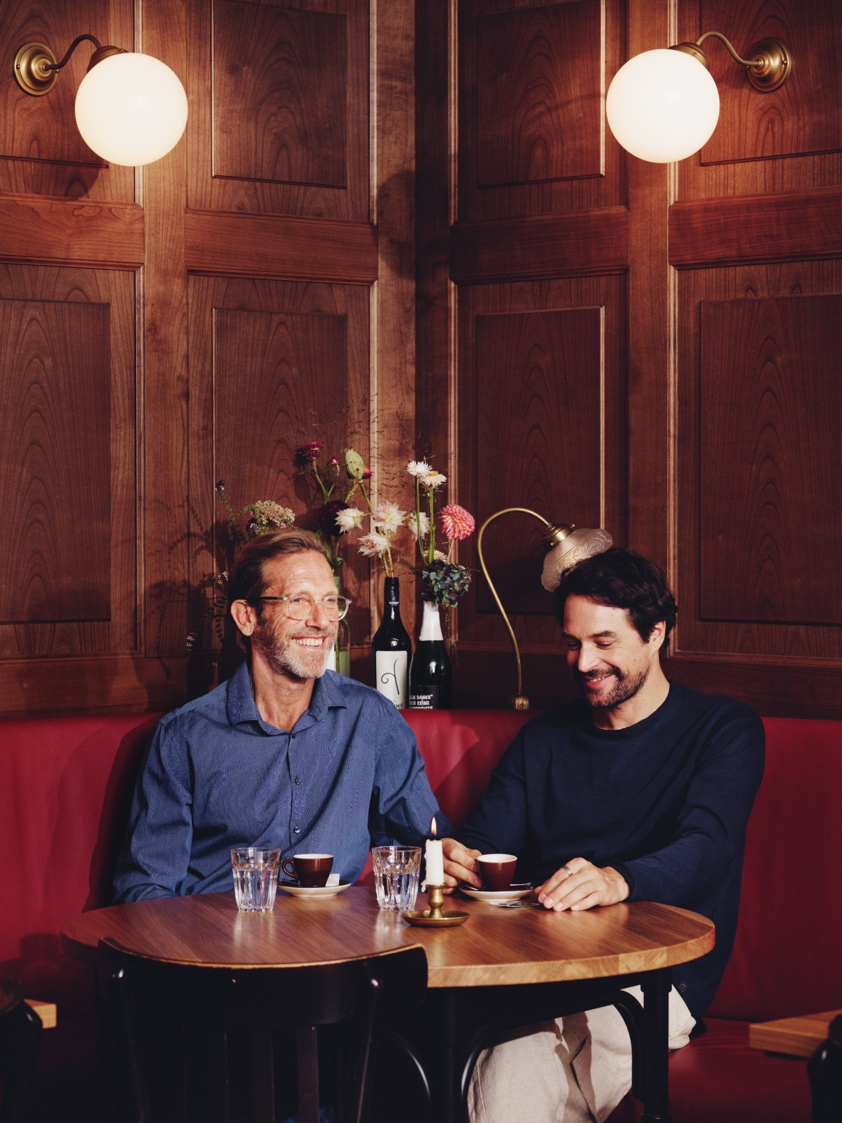 Zwei Männer sitzen an einem Tisch mit Kaffeetassen in einem gemütlichen Restaurant mit Holzwänden.